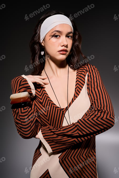 Preview: Young woman in striped dress showcases contemporary design in studio setting