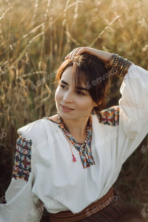 Preview: Young woman in traditional national embroidered shirt and skirt on nature at sunset.