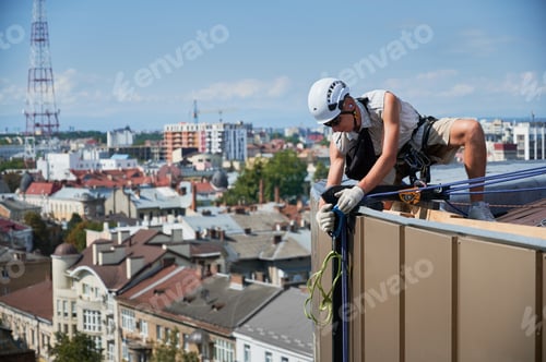 Preview: Industrial mountaineering worker cleaning window outside building.