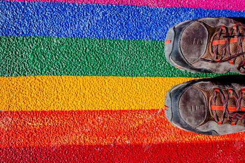 Preview: A man steps on his boots with the gay flag, painted on the ground, a concept of contempt for rights.