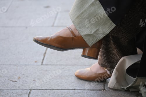 Preview: Person wearing brown heels sits on pavement in city