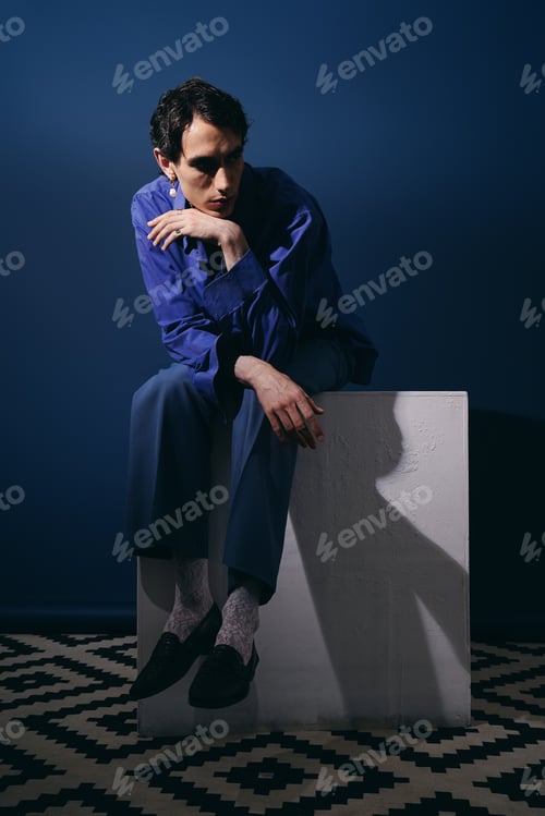 Preview: Stylish man poses thoughtfully in a modern setting with rich blue backdrop