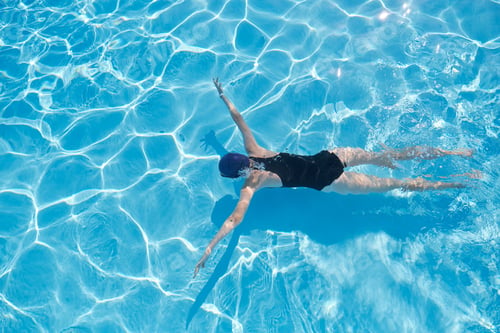 Preview: Young woman swimming underwater in an outdoor pool, top view of back of girl