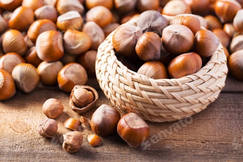 Preview: Basket of hazelnuts on wooden table with scattered nuts around in natural light