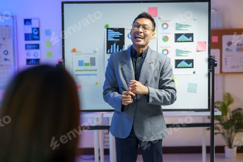 Preview: Asian businessman is holding a pen and smiling while presenting a business plan using a whiteboard