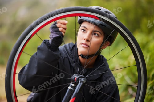 Preview: One athletic young woman fixing the wheel of a bike while cycling outdoors. Sporty female wearing h