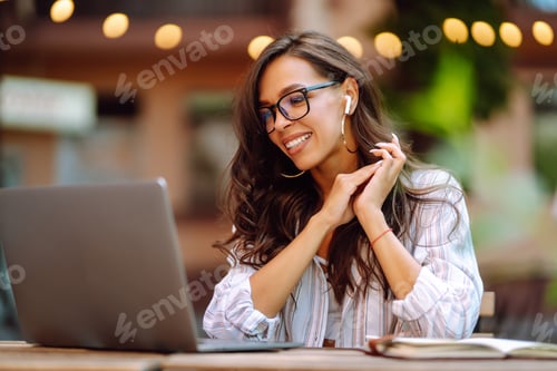 Preview: Young woman with wireless headphones calling on laptop, talk by webcam, video conference on cafe.