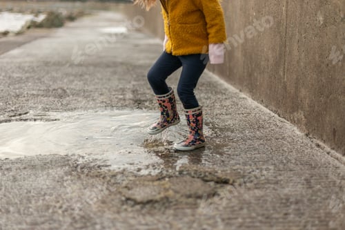 Preview: A little girl with rubber boots jumps into a puddle on a rainy day