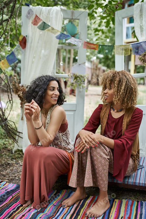 Preview: smiling multiethnic women in boho outfits talking while spending time outdoors in retreat center