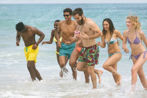 Preview: Front view of multi ethnic group of friends enjoying and running on sea at beach on sunny day