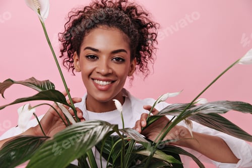 Preview: Curly girl smiling and posing with plant on isolated background. Brunette woman in white shirt hold