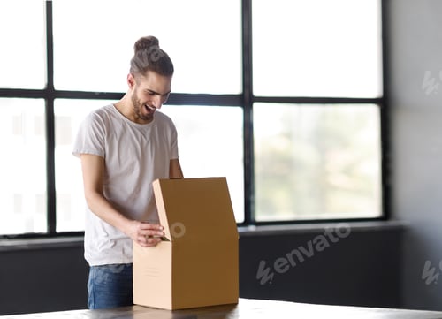 Preview: Joyful Young Hispanic Man Opening Box Unboxing Parcel At Workplace