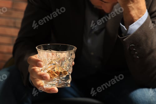 Preview: Addicted man with glass of alcoholic drink near red brick wall, closeup