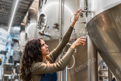 Preview: Woman brewer checking craft beer quality in tank
