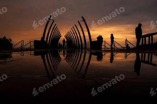 Preview: Silhouettes of people on a modern bridge, reflecting on wet ground at sunset