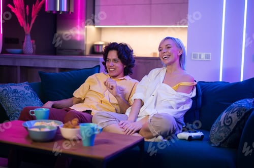 Preview: Couple of young adults playing video games at home. Emotional diverse gamers holding joysticks and