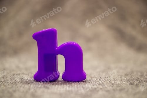 Preview: Closeup shot of a plastic purple-colored lower case letter ''h'' on a playroom carpet