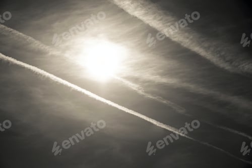 Preview: The Bright White Sun And Traces From Gray Exhausts Of Jet Planes In The Dark Beige Sky