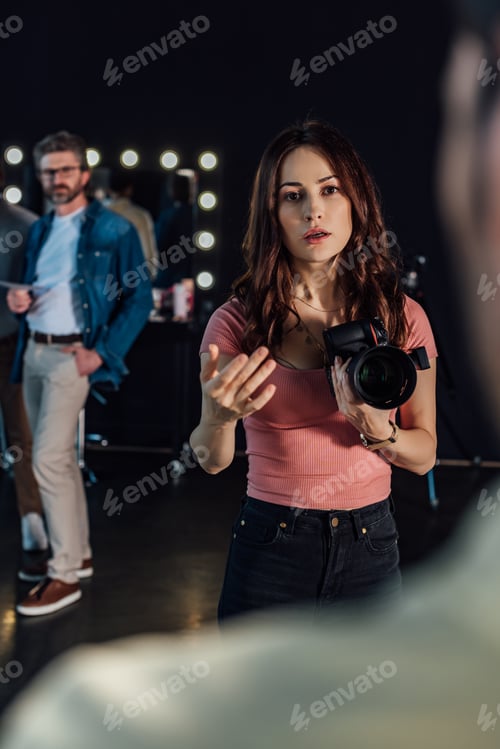 Preview: selective focus of attractive photographer speaking while gesturing and looking at man in photo
