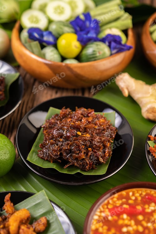 Preview: Chili paste is served on banana leaves on a plate with long beans, lime, chili, and eggplant.