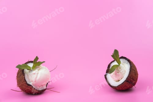 Preview: Vanilla ice cream balls in fresh coconut halves decorated with mint leaves on a pink background