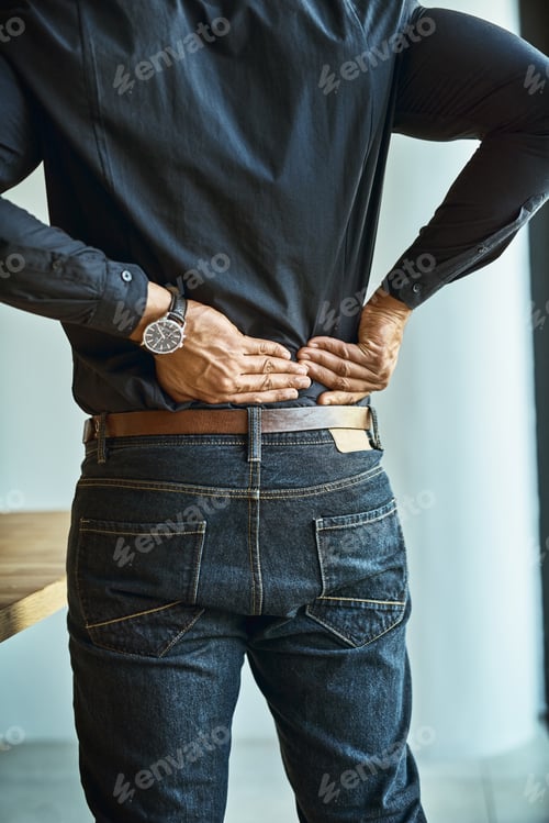 Preview: Shot of a young businessman suffering from back pain while working in an office