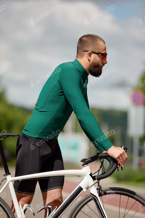 Preview: Portrait of a sporty man in a cycling outfit standing with a bicycle on the Bike Lane, posing for