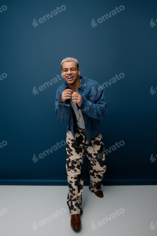 Preview: Young Black man poses stylishly in denim against a blue backdrop