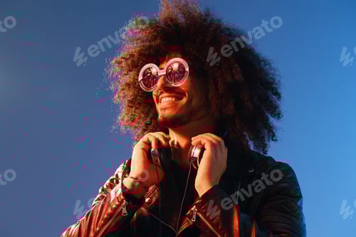 Preview: Portrait of a stylish man with curly hair with glasses and headphones on a blue background