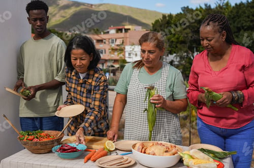 Preview: Group of multiracial friends having fun preparing food for barbecue dinner at house rooftop