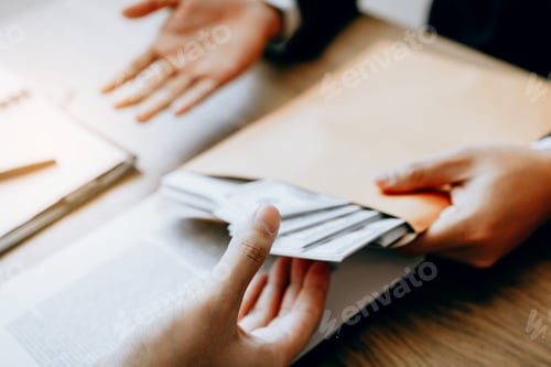Preview: Businessman secretly giving a bribe by giving money bills in envelope contract document.