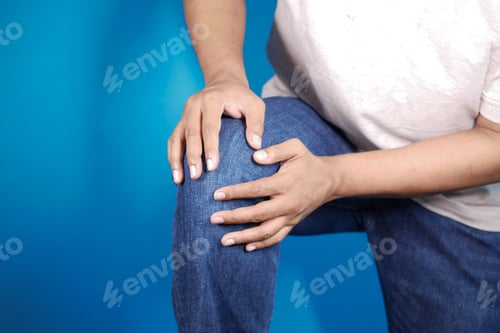 Preview: young man holding his knee for suffering joint pain against blue background