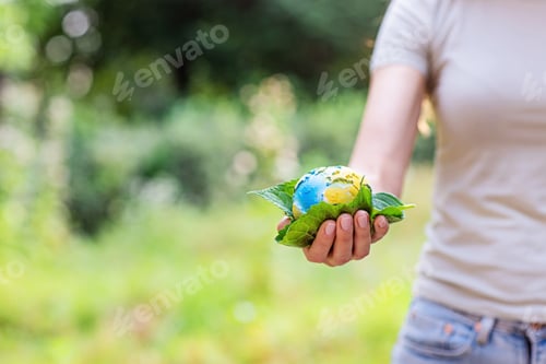 Preview: Young woman holding small planet in hands against spring or summer green background with copy space
