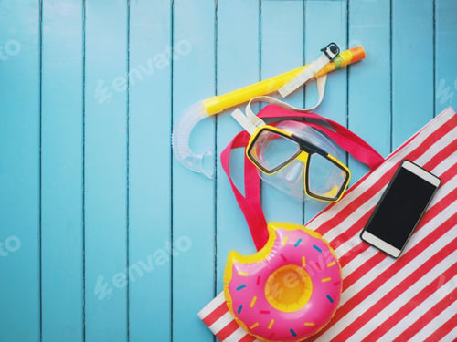 Preview: Top view of yellow snorkeling ,beach bag,smart phone and balloons float on wooden texture.