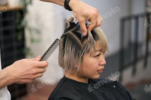 Preview: Hairdresser combing and sectioning hair of young woman in salon