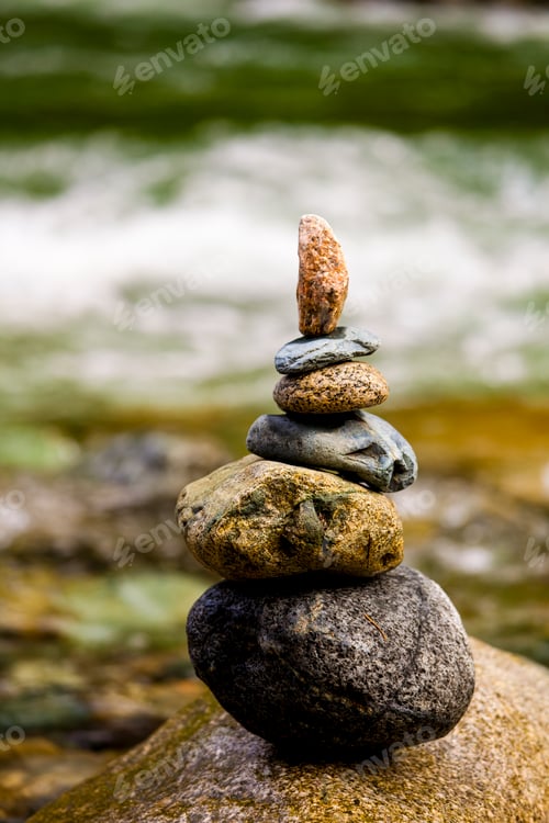 Preview: A stack of small rocks balanced on top of each other by a river.