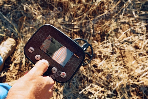 Preview: Male hand holding metal detector device above the ground