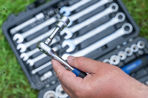 Preview: Man's hand holds a metal tool over a box with a set of tools supplies for construction work closeup