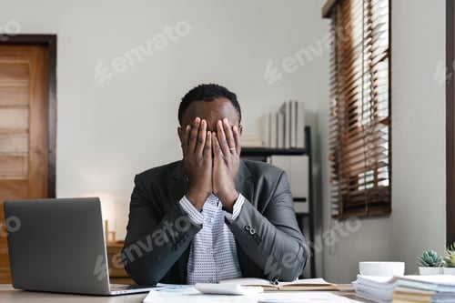 Preview: Stressed business man sitting at office workplace. Tired and overworked black man. Young african