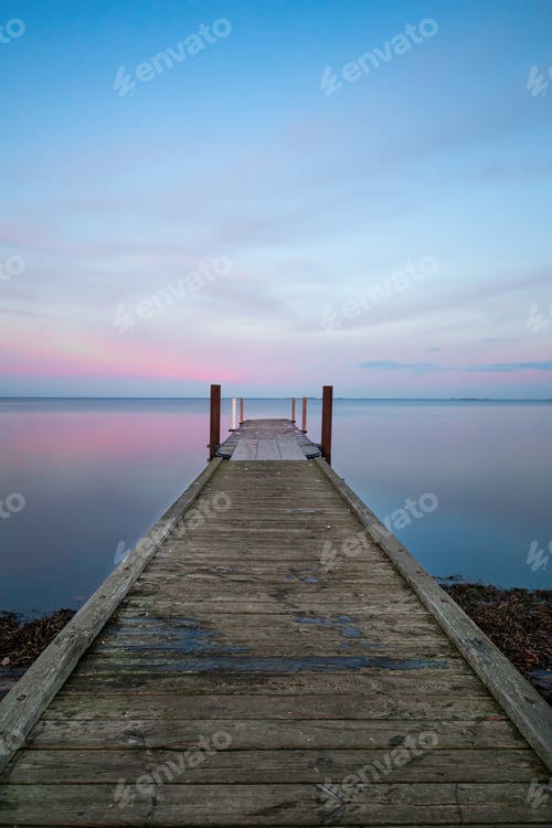 Preview: Vertical shot of a long wooden pier near the ocean under the pastel-colored sky