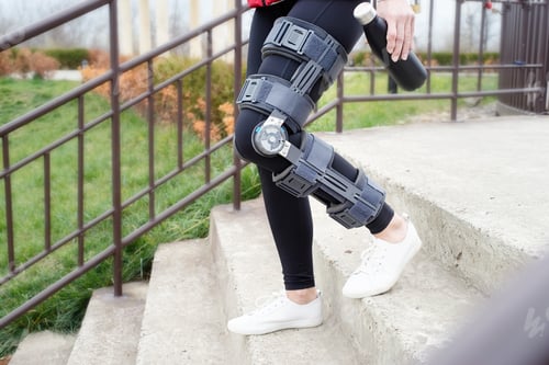 Preview: Woman wearing knee brace or orthosis after leg surgery, walking in the park