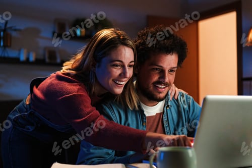 Preview: Young happy caucasian couple browsing on internet using a laptop to search sale at home. Excited
