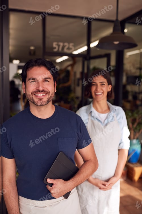 Preview: Portrait Of Male And Female Owners Of Florists With Digital Tablet Standing In Doorway With Plants