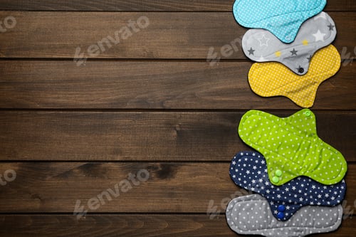 Preview: Many reusable cloth menstrual pads on wooden table, flat lay. Space for text