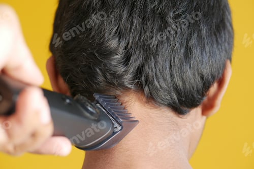 Vista previa: cutting hair with a hair-clipper on yellow background
