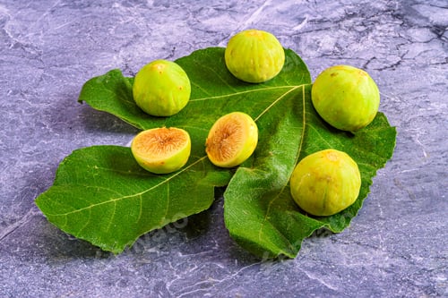 Preview: Fresh green figs on fig leaves on marble