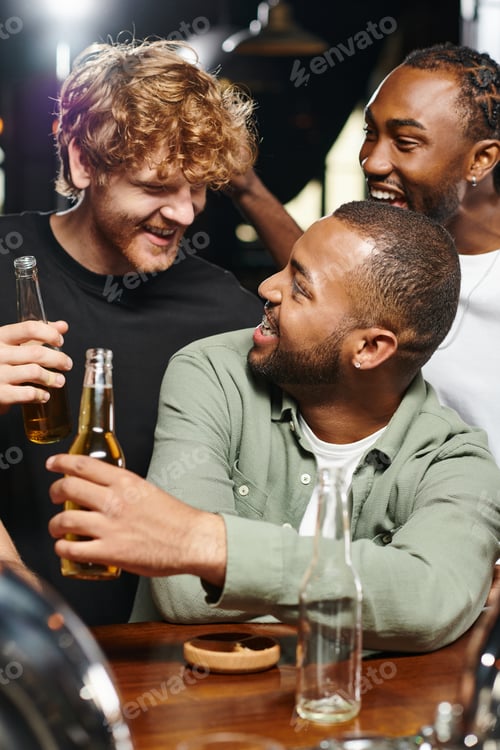 Preview: three joyful multiethnic friends smiling and toasting glasses of beer while spending time in bar