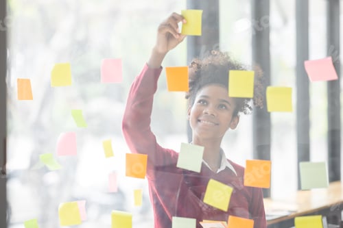 Preview: Young mixed african american businesswoman with afro hairstyle planning on whiteboard in a startup