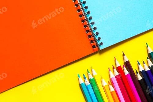 Preview: Rainbow palette of colored pencils with a spiral notebook on a yellow background