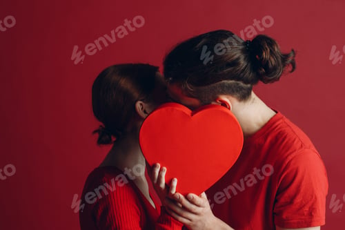 Preview: Man and woman young couple kissing and hiding behind heart-shaped box